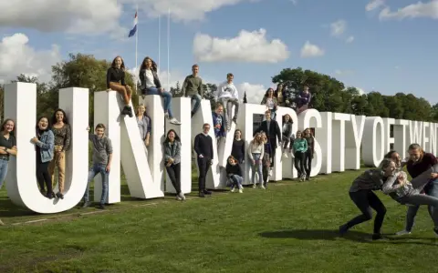 Un groupe d'étudiants pose joyeusement devant les lettres géantes "UNIVERSITY OF TWENTE".