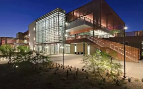 Bâtiment moderne d'un college aux États-Unis, avec une façade vitrée et des escaliers extérieurs en bois, éclairé la nuit.