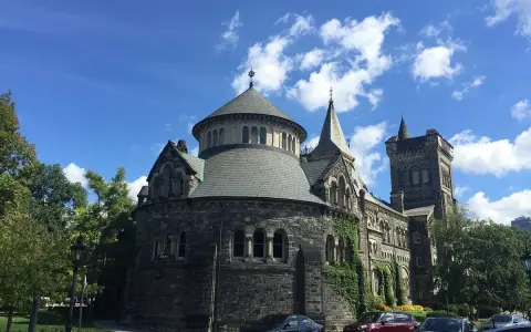 Bâtiment historique en pierre, rappelant une école de cinéma à Toronto, sous un ciel bleu et nuageux.