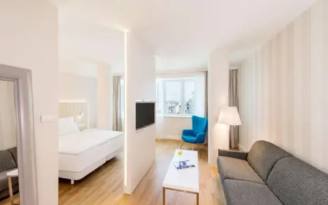 Chambre moderne avec lit, canapé, TV et vue sur la ville. Idéal pour un logement étudiant à Vienne, Autriche.
