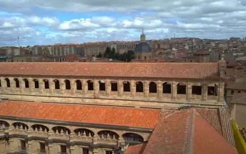 Vue aérienne de l'université pontificale de Salamanque, avec ses toits de tuiles rouges et son dôme emblématique sous un ciel nuageux.
