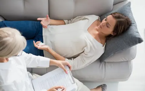 Une femme en thérapie, allongée sur un canapé, discute avec sa psychologue. Une scène qui pourrait inspirer un futur master psychologie à l'étranger.