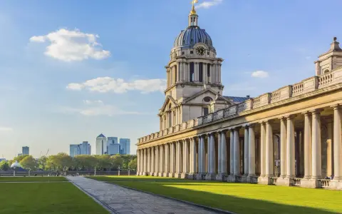 Le bâtiment néoclassique de l'université de Greenwich, avec son dôme et ses colonnes imposantes, se dresse sous un ciel bleu clair.
