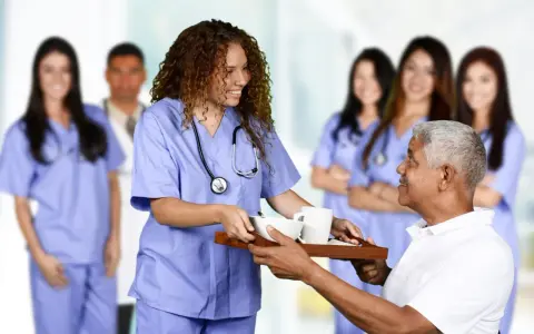 Une jeune femme en formation paramédicale sans bac, souriante, sert un plateau repas à un patient.