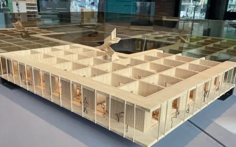 Maquette en bois d'une école d'architecture belge, avec des figures stylisées et des plantes.