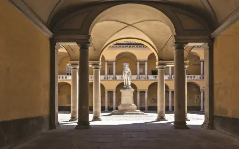 Cour intérieure de l'université de Pavie, avec une statue au centre, entourée d'arcades et de colonnes.