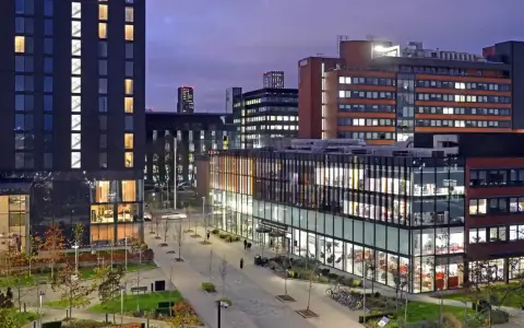 Bâtiments modernes illuminés le soir, avec une enseigne Alliance Manchester Business School visible.