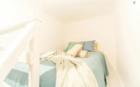Lit douillet dans un logement étudiant à Budapest, avec des coussins bleus et verts, et des plaids beiges.