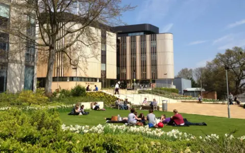 Étudiants profitant du soleil sur la pelouse devant le bâtiment de la **université de Southampton**.