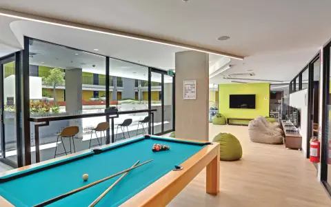 Salle commune moderne pour logement étudiant à Sydney, avec table de billard, poufs et espace extérieur visible.