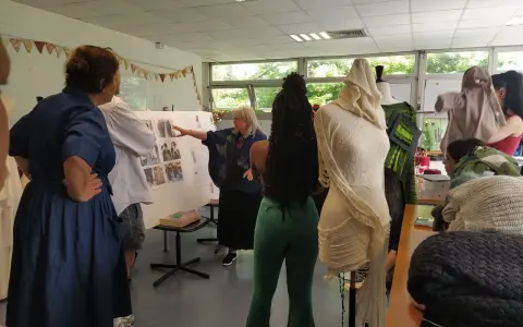 Des élèves d'une école de mode gratuite présentent leurs créations sur des mannequins. Une enseignante explique un tableau d'inspiration.