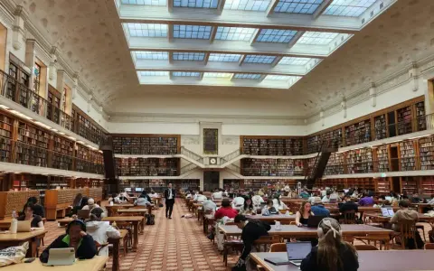 Vaste bibliothèque avec étudiants travaillant sur leurs ordinateurs portables, un décor idéal pour une licence science politique à distance.