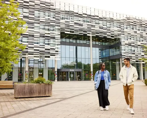 Deux étudiants marchent devant l'université métropolitaine de Manchester, un bâtiment moderne avec une façade à motifs.