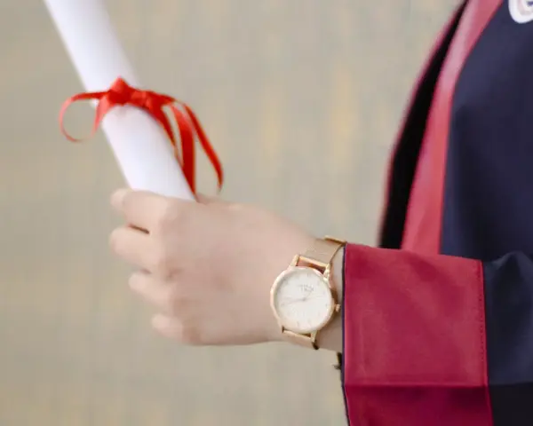 Main tenant un diplôme, une personne porte une robe de doctorat en anglais.