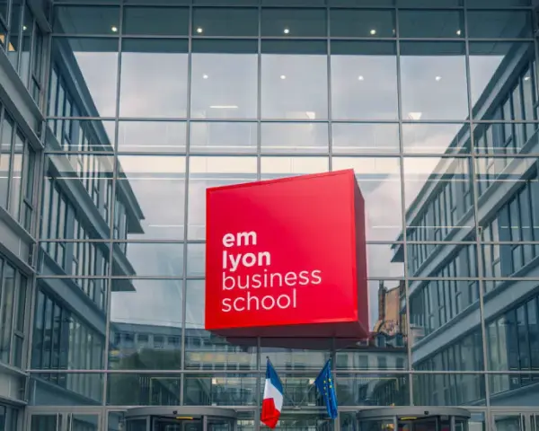 Le logo rouge d'EM Lyon Business School flotte devant un bâtiment moderne en verre. Idéal pour un master project management.