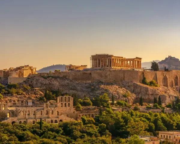 L'Acropole d'Athènes baignée de soleil, un site historique qui rappelle le coût de la vie en Grèce, entre ruines antiques et verdure luxuriante.