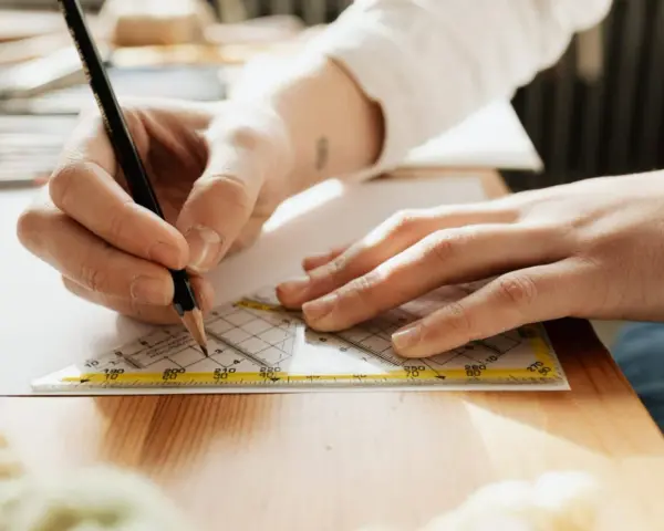 Main d'un étudiant en BTS Design d'Espace à Paris traçant une ligne précise avec un crayon et une équerre sur une feuille.