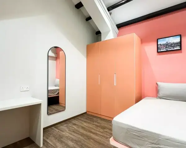 Chambre moderne pour **logement étudiant à Singapour** : lit, bureau, armoire corail et miroir mural.