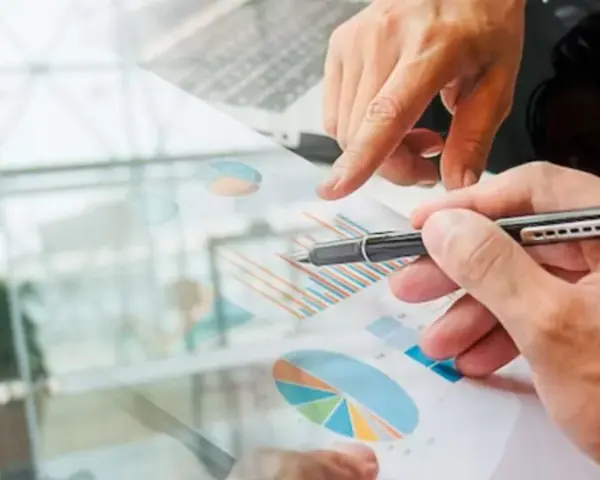Un homme en costume regarde des graphiques financiers. Des mains analysent des données, suggérant une licence finance à distance.