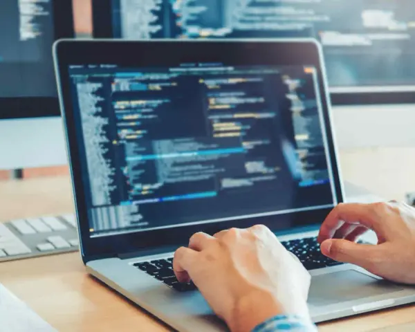 Des mains tapant sur un clavier d'ordinateur portable affichant du code. Une opportunité de formation informatique sans bac pour un avenir prometteur.