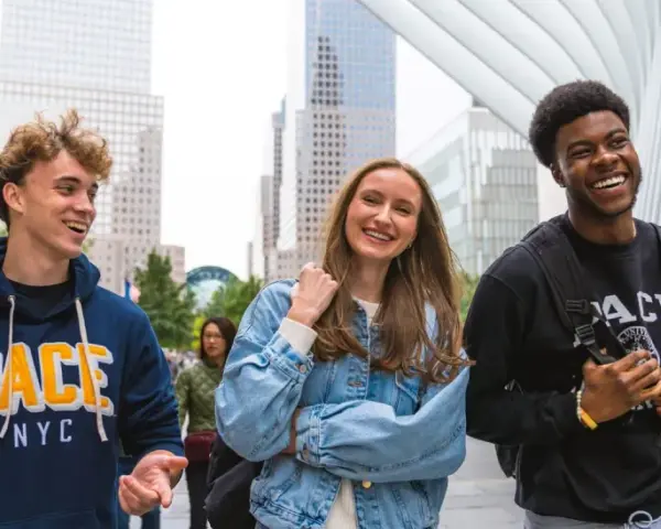 Trois étudiants souriants marchent dans le quartier financier de New York, un lieu idéal pour un MBA.