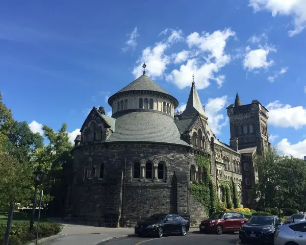 Bâtiment historique en pierre, rappelant une école de cinéma à Toronto, sous un ciel bleu et nuageux.