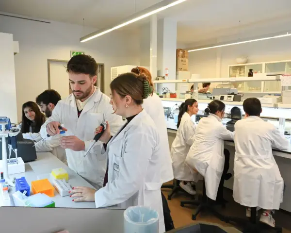 Des étudiants en blouse blanche travaillent dans un laboratoire de l'école vétérinaire de Porto, manipulant des pipettes et des éprouvettes.