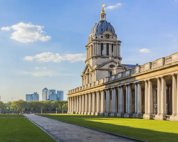 Le bâtiment néoclassique de l'université de Greenwich, avec son dôme et ses colonnes imposantes, se dresse sous un ciel bleu clair.