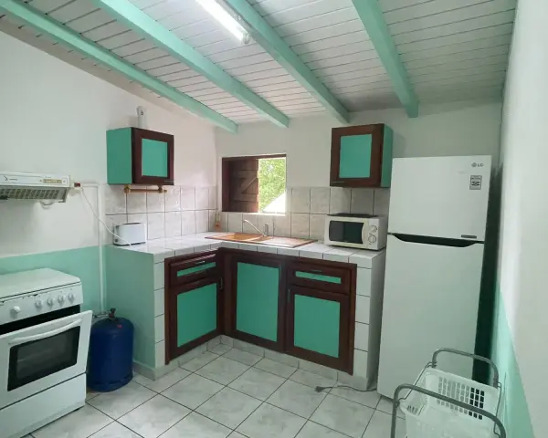 Cuisine fonctionnelle pour un logement étudiant en Guadeloupe : cuisinière, réfrigérateur, micro-ondes, évier et rangements.