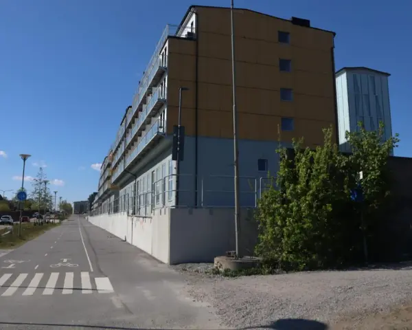 Immeuble moderne avec balcons vitrés, idéal pour le logement étudiant à Stockholm. Une piste cyclable longe le bâtiment.