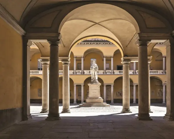 Cour intérieure de l'université de Pavie, avec une statue au centre, entourée d'arcades et de colonnes.