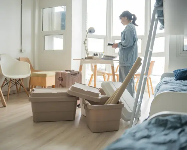 Une jeune femme déballe ses affaires dans une chambre d'étudiant au Canada. Valises et boîtes sont empilées, prête pour une nouvelle vie.