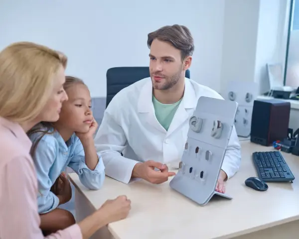 Un audioprothésiste explique des appareils auditifs à une mère et sa fille. Une scène qui pourrait illustrer la formation accélérée audioprothésiste.