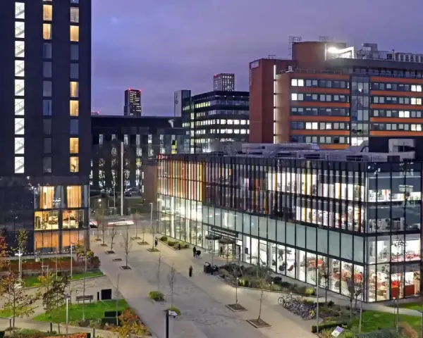 Bâtiments modernes illuminés le soir, avec une enseigne Alliance Manchester Business School visible.