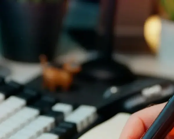 Main tenant une plume, prêt à étudier pour sa licence sociologie à distance. Un clavier mécanique et une petite figurine complètent le décor.