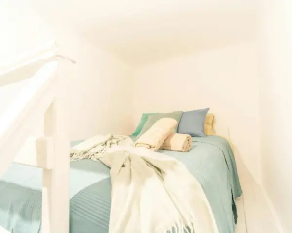 Lit douillet dans un logement étudiant à Budapest, avec des coussins bleus et verts, et des plaids beiges.