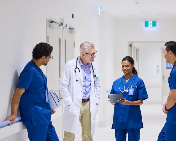 Une équipe médicale discute dans un couloir d'hôpital. Un médecin en blouse blanche échange avec trois infirmiers en uniforme bleu. Ils semblent discuter d'un cas, peut-être en lien avec du infirmier en ligne.