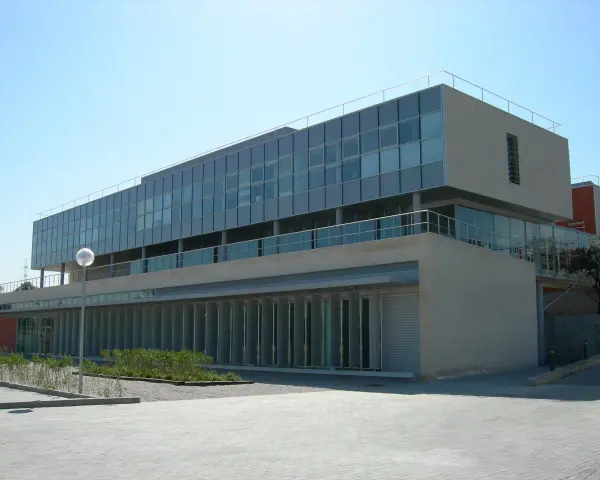 Bâtiment moderne aux lignes épurées, possiblement une école d'élite à Madrid, avec de grandes baies vitrées et une façade en pierre claire.