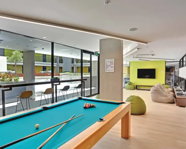 Salle commune moderne pour logement étudiant à Sydney, avec table de billard, poufs et espace extérieur visible.
