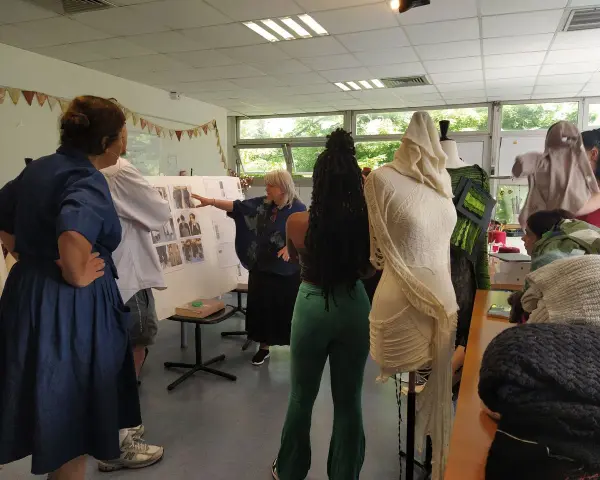 Des élèves d'une école de mode gratuite présentent leurs créations sur des mannequins. Une enseignante explique un tableau d'inspiration.