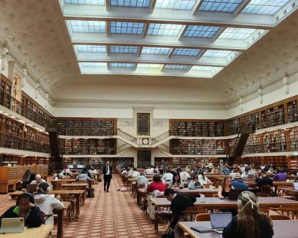 Vaste bibliothèque avec étudiants travaillant sur leurs ordinateurs portables, un décor idéal pour une licence science politique à distance.