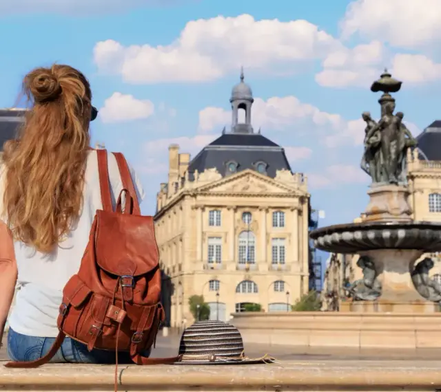 Jeune femme avec un sac à dos en cuir, profitant de sa **année de césure** à Bordeaux, devant la fontaine de la Place de la Bourse.