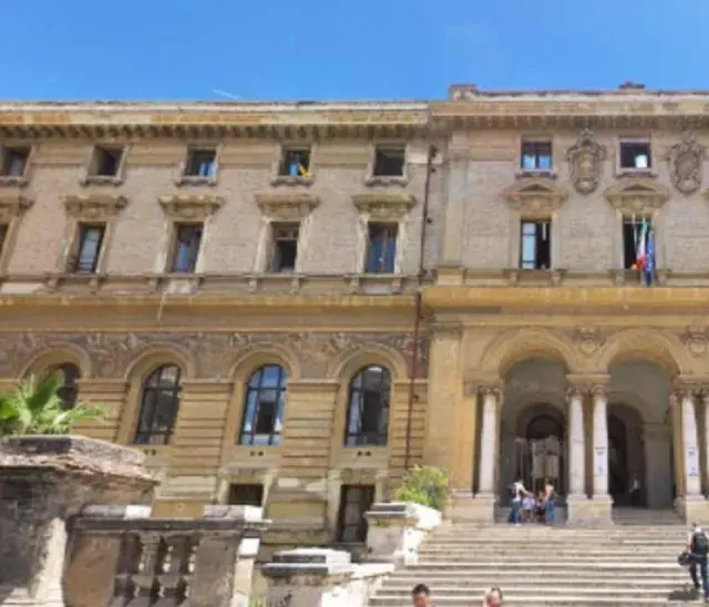 Grand bâtiment à Rome, avec une entrée imposante et des drapeaux italiens. Un lieu pour master Rome.