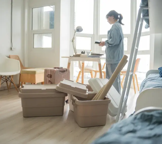 Une jeune femme déballe ses affaires dans une chambre d'étudiant au Canada. Valises et boîtes sont empilées, prête pour une nouvelle vie.