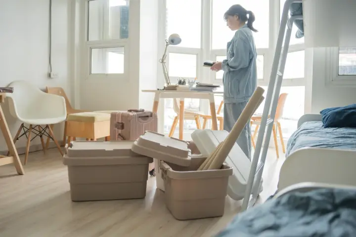 Une jeune femme déballe ses affaires dans une chambre d'étudiant au Canada. Valises et boîtes sont empilées, prête pour une nouvelle vie.