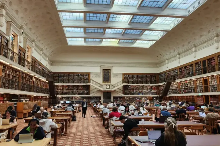 Vaste bibliothèque avec étudiants travaillant sur leurs ordinateurs portables, un décor idéal pour une licence science politique à distance.
