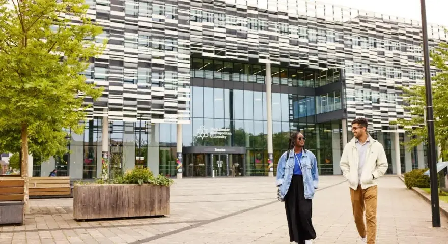 Deux étudiants marchent devant l'université métropolitaine de Manchester, un bâtiment moderne avec une façade à motifs.