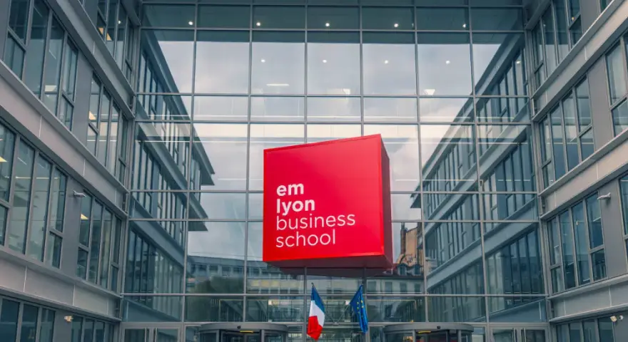 Le logo rouge d'EM Lyon Business School flotte devant un bâtiment moderne en verre. Idéal pour un master project management.