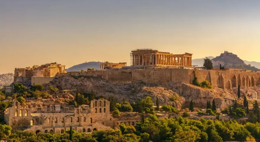 L'Acropole d'Athènes baignée de soleil, un site historique qui rappelle le coût de la vie en Grèce, entre ruines antiques et verdure luxuriante.