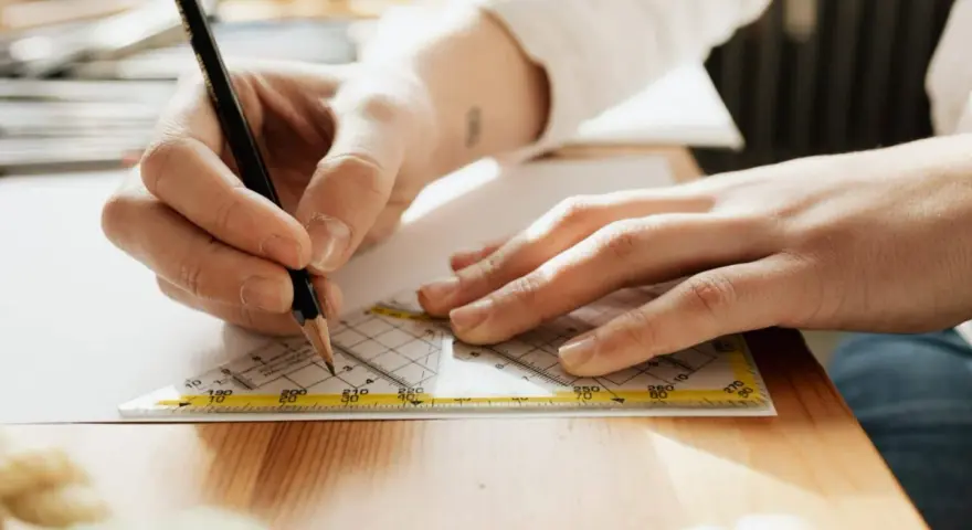 Main d'un étudiant en BTS Design d'Espace à Paris traçant une ligne précise avec un crayon et une équerre sur une feuille.